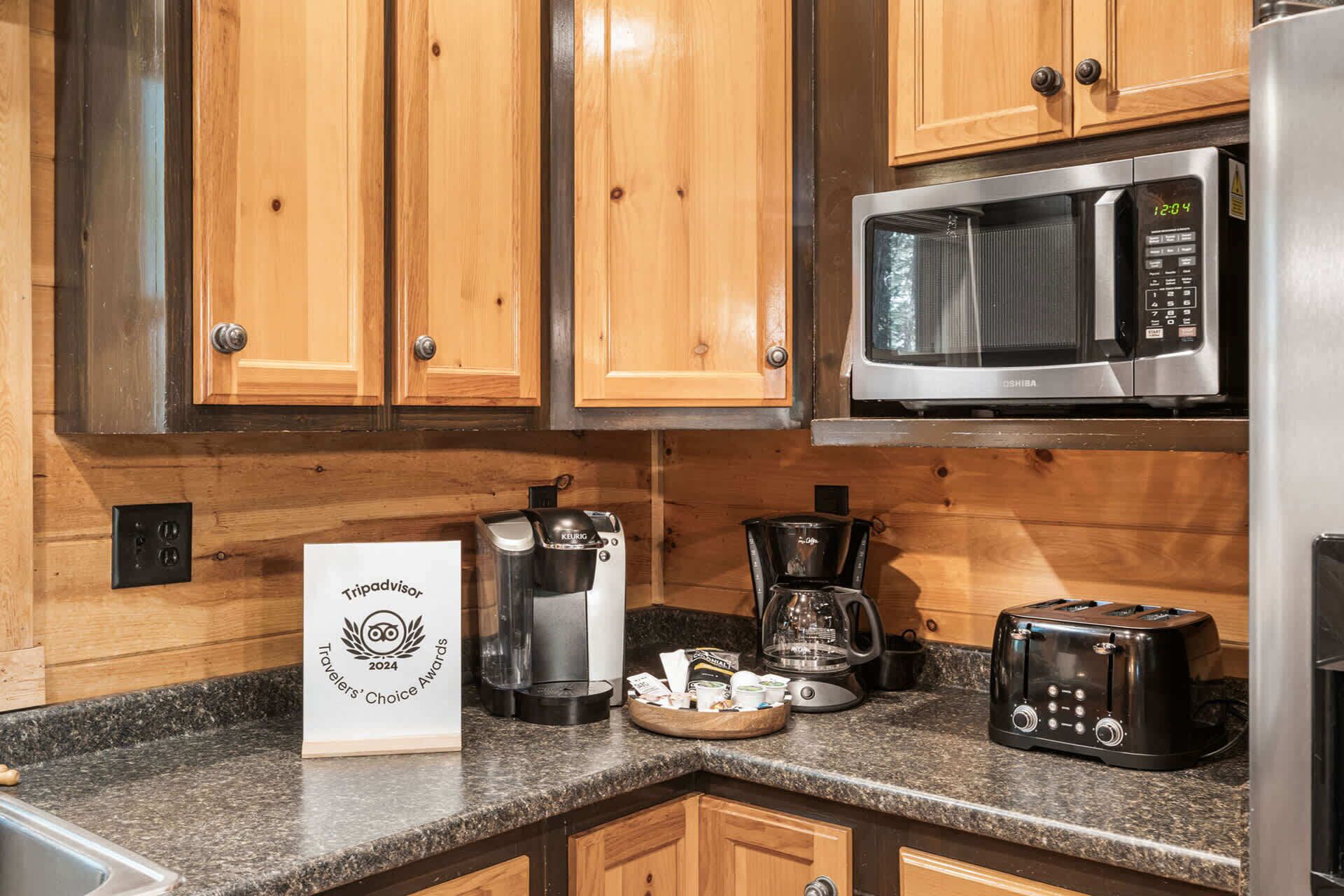 A kitchen with wooden cabinets, a stainless steel microwave, a coffee maker, a toaster, and a sign indicating a TripAdvisor award.