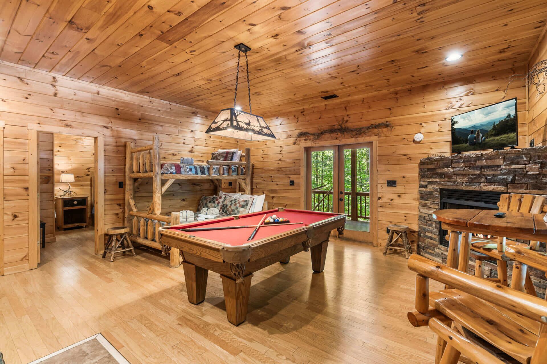 Het interieur van een houten chalet met een pooltafel, een stenen open haard en een aan de muur bevestigde televisie.
