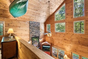 Ein Holzblockhaus-Interieur mit Kamin, großen Fenstern und einem Fernseher.