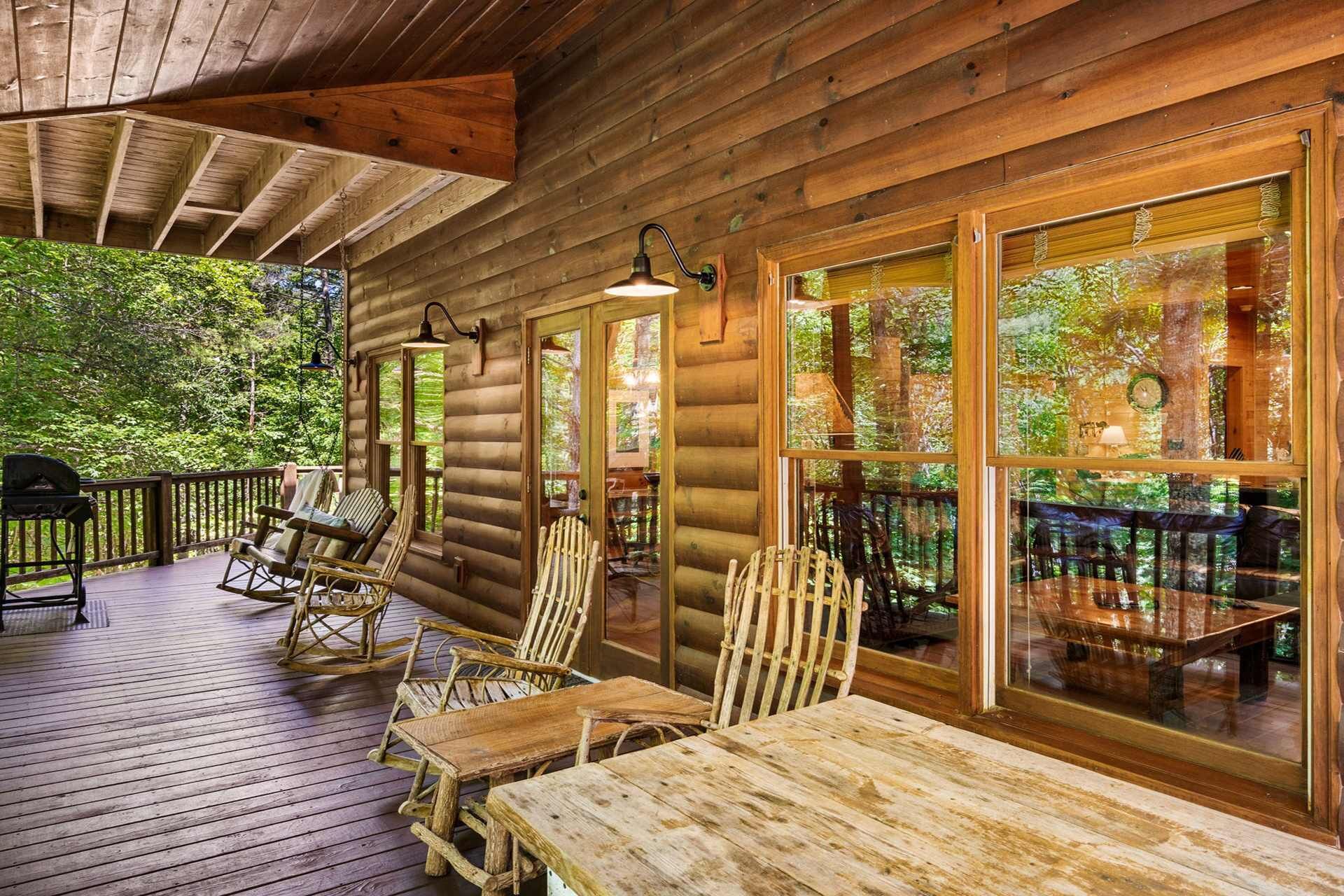 A log cabin with a wooden deck, rocking chairs, and a table.