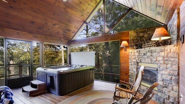 A cozy cabin interior with a stone fireplace, a hot tub, and large windows offering a view of the surrounding forest. - Hot Tub & Scenic Mountain Views, Game Room (Mineral Bluff)