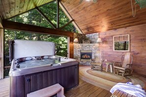 A wooden cabin with a hot tub, stone fireplace, and rustic furniture.