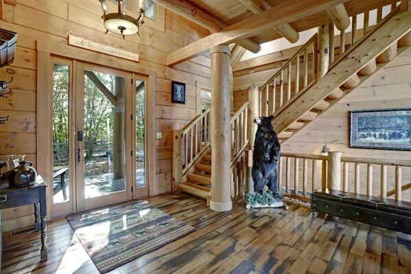 A wooden interior with a staircase, a bear statue, and a framed picture on the wall.