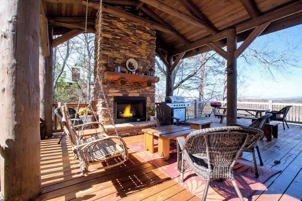 A covered outdoor deck with a stone fireplace, wicker furniture, and a grill.