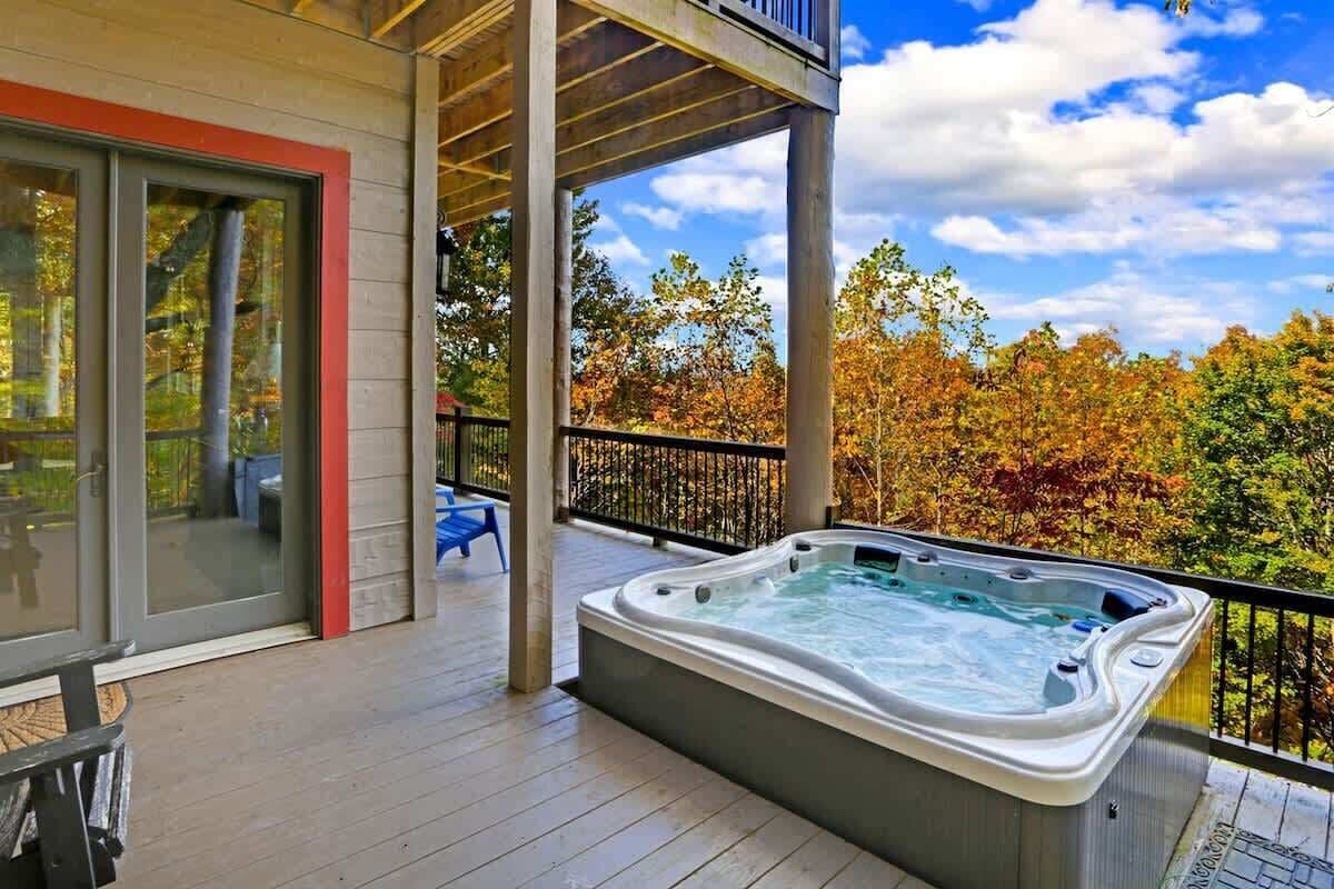 A hot tub on a wooden deck with a glass door and a view of autumn trees.