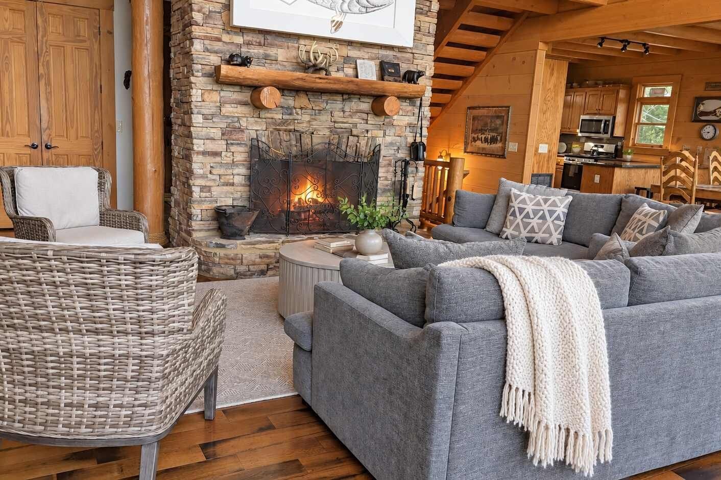 A cozy living room with a stone fireplace, grey sofas, and a wicker chair.