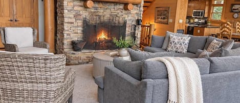 A cozy living room with a stone fireplace, grey sofas, and a wicker chair.