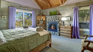 Une chambre confortable avec un lit, une cheminée en pierre, une télévision et une commode.