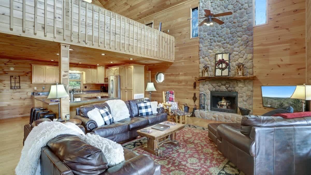 A spacious living area with a stone fireplace, leather sofas, and a high ceiling with exposed beams.