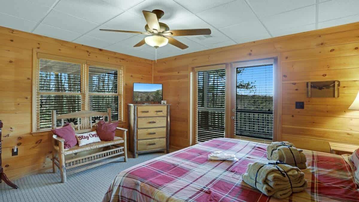 A wooden cabin bedroom with a bed, a dresser, a bench, and a ceiling fan.