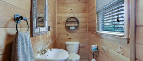 A wooden-paneled bathroom with a sink, toilet, and window with blinds.