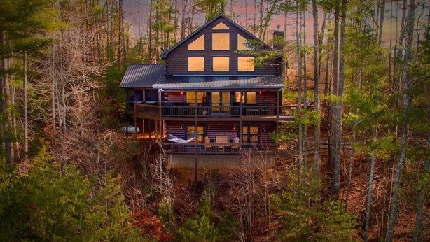 A two-story log cabin with a balcony, surrounded by dense forest. - Stunning Mountain Sunset Views, screened-in HotTub (Mineral Bluff)