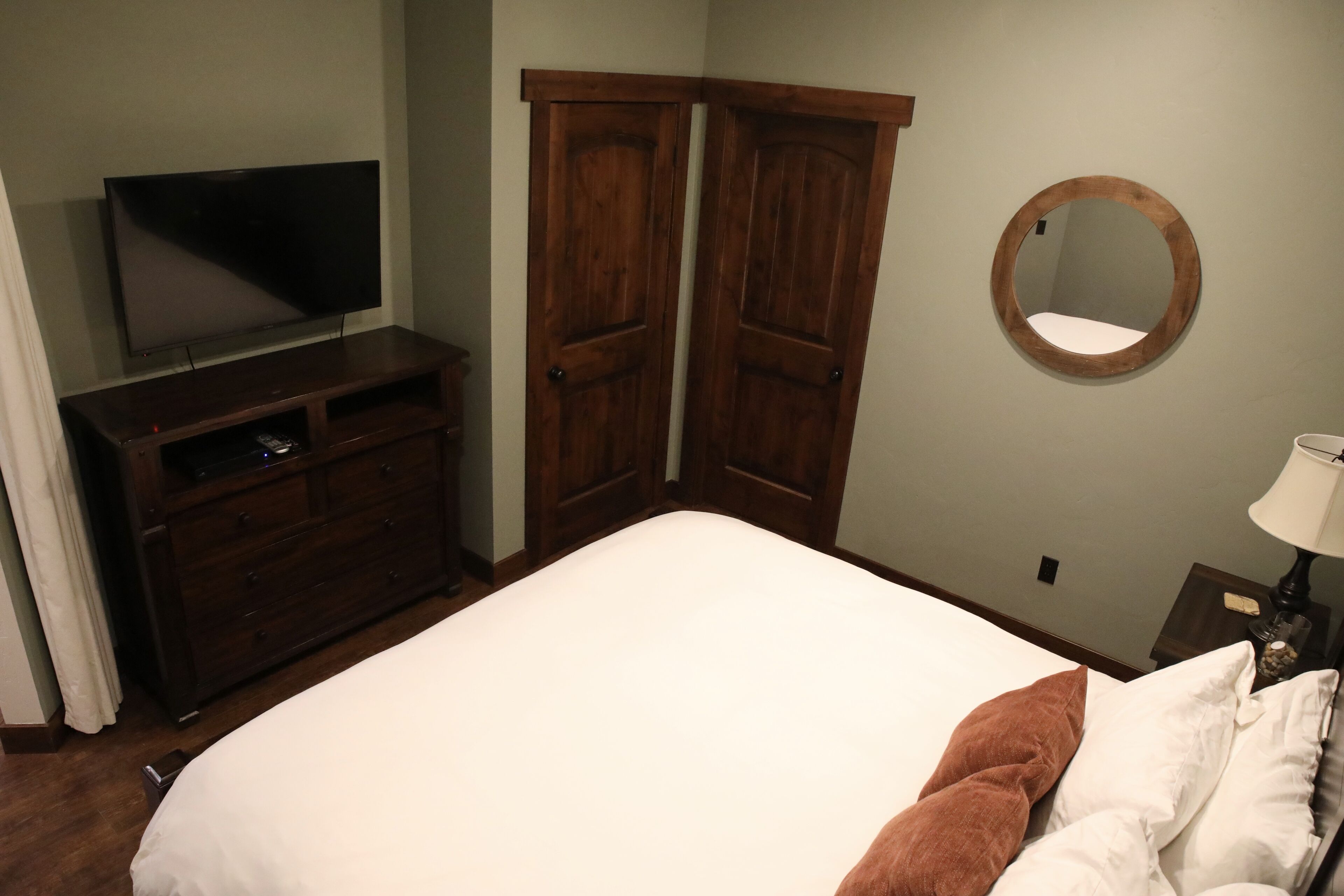 Een slaapkamer met een bed, een kaptafel, een televisie, een spiegel en een nachtkastje met een lamp.