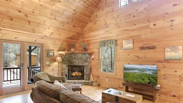 L’intérieur chaleureux d’un chalet avec une cheminée en pierre, un canapé en cuir et un téléviseur diffusant un paysage magnifique.