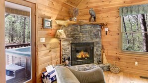 L’intérieur chaleureux d’un chalet avec une cheminée en pierre, des murs en bois et une vue sur la forêt par la fenêtre.