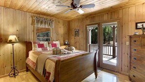 A wooden-paneled bedroom with a bed, a nightstand, a lamp, a dresser, and a door leading outside. - Secluded Cabin w/ Hot Tub & Cozy Fire Pit (Morganton)