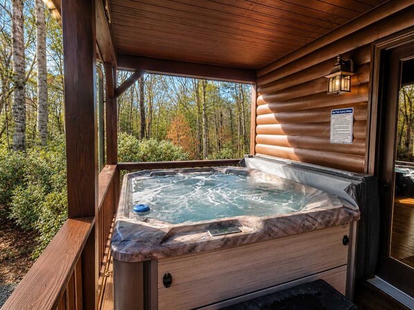 Een hottub met een houten terras en uitzicht op een bos.
