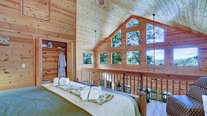 A wooden cabin bedroom with a bed, a wardrobe, and a balcony with a railing. - Romantic Cabin w/ Hot Tub & Grand Fire Pit (Mineral Bluff)