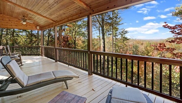 A covered outdoor deck with lounge chairs and a table, overlooking a forested landscape. - Romantic Cabin w/ Hot Tub & Grand Fire Pit (Mineral Bluff)
