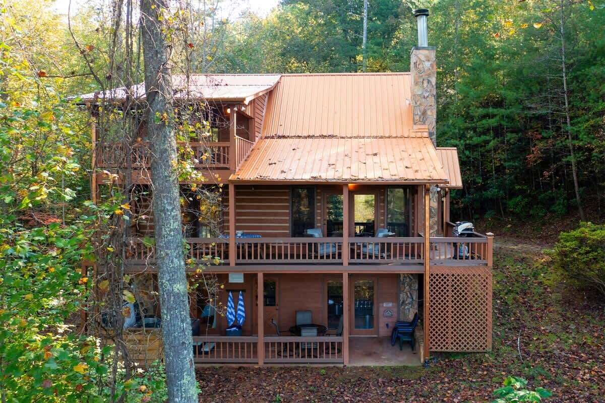 A two-story cabin with a balcony, surrounded by trees.
