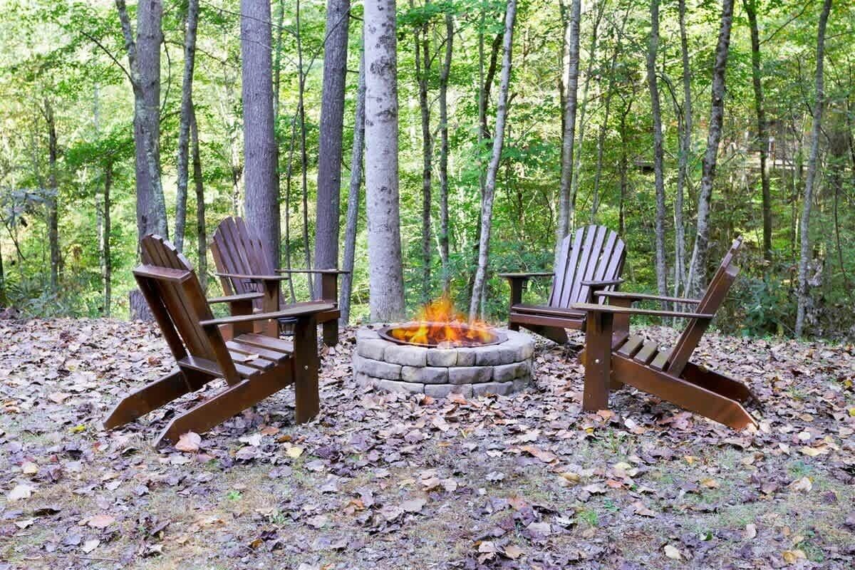 Dos sillas Adirondack alrededor de un brasero de piedra en un entorno boscoso.