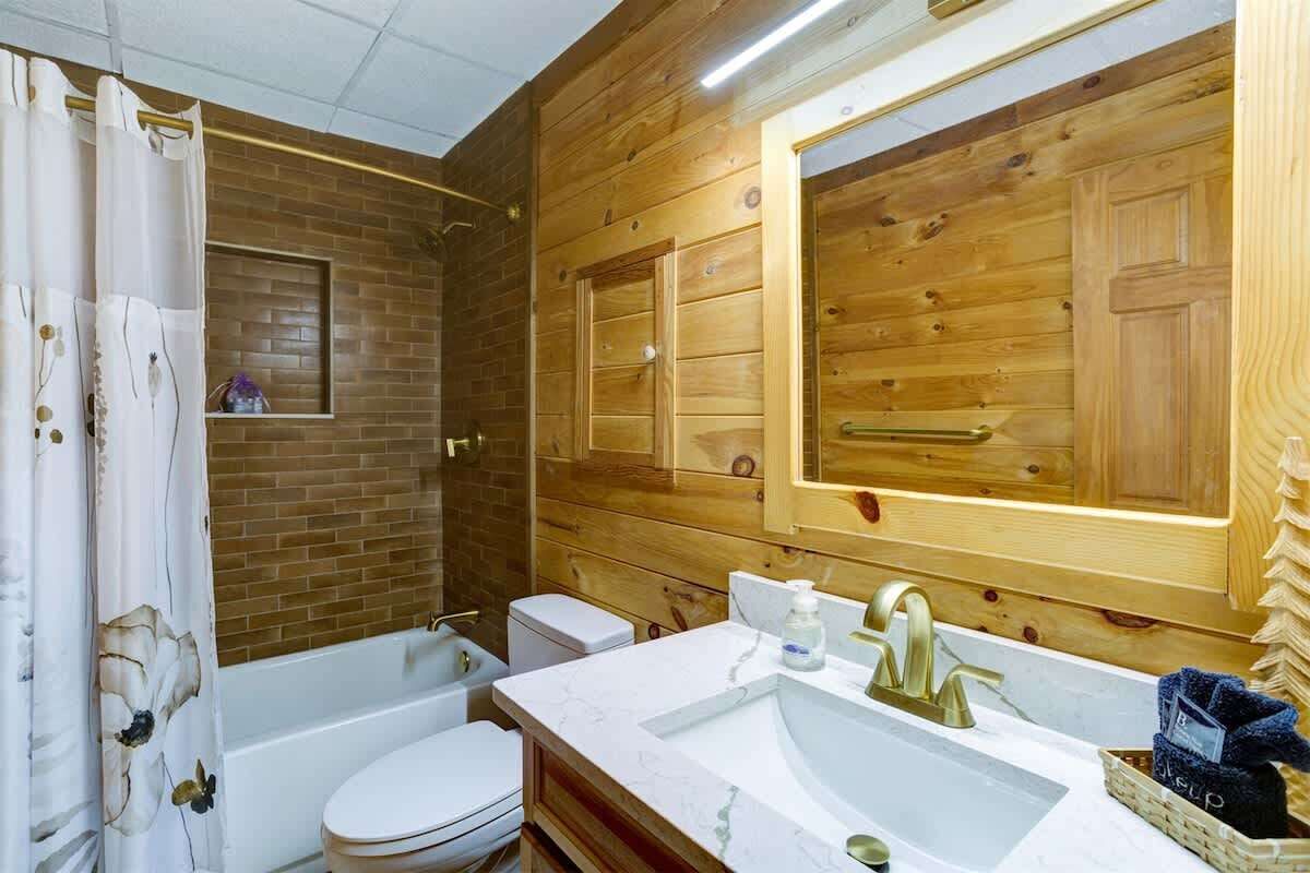 Ein Badezimmer mit Holzwand, einer weißen Badewanne, einer Toilette und einem Waschbecken mit Spiegel darüber.