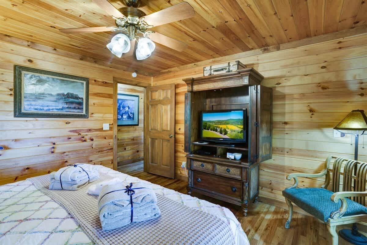 Una habitación de madera con una cama, televisión, una silla y un ventilador de techo.