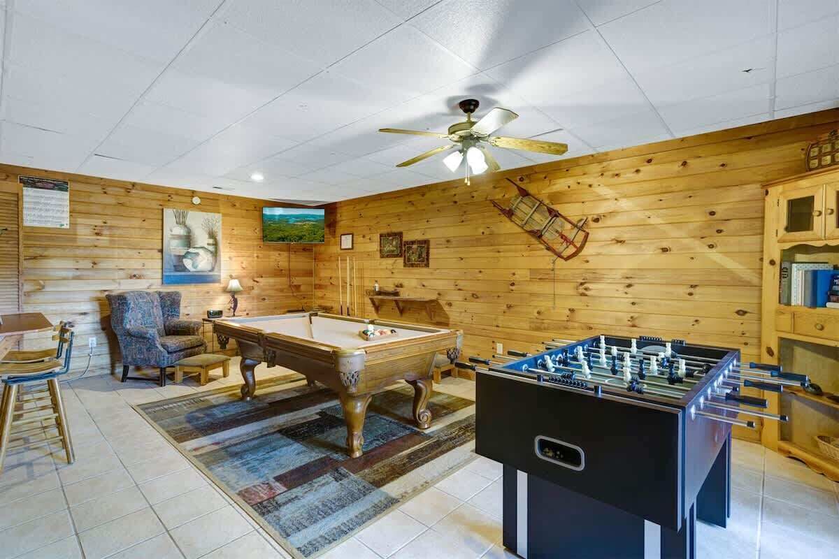A room with a pool table, foosball table, and a ceiling fan.