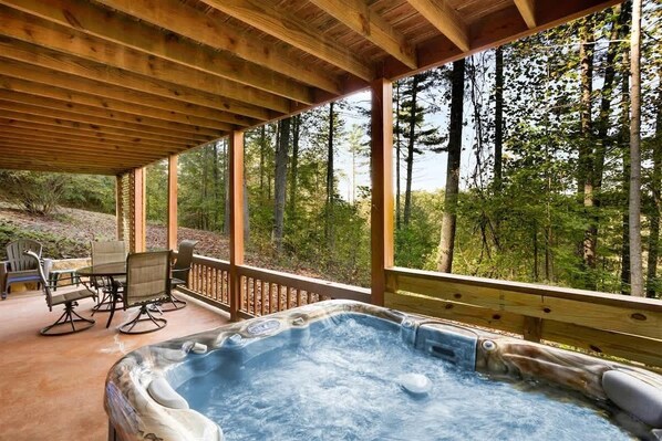 A hot tub under a wooden deck with a view of a forested area. - Secluded Cabin w/ Hot Tub & Game Room (Morganton)