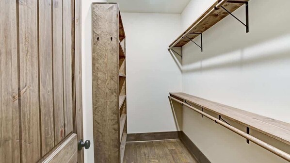 Un pasillo estrecho con suelo de madera, una puerta de madera y estanterías empotradas en la pared derecha.