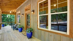 Eine überdachte Veranda mit Holzboden, großen Fenstern und Topfpflanzen.