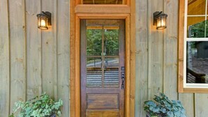 Eine Holztür mit Fenster, zwei Wandleuchten und Blumentöpfen.