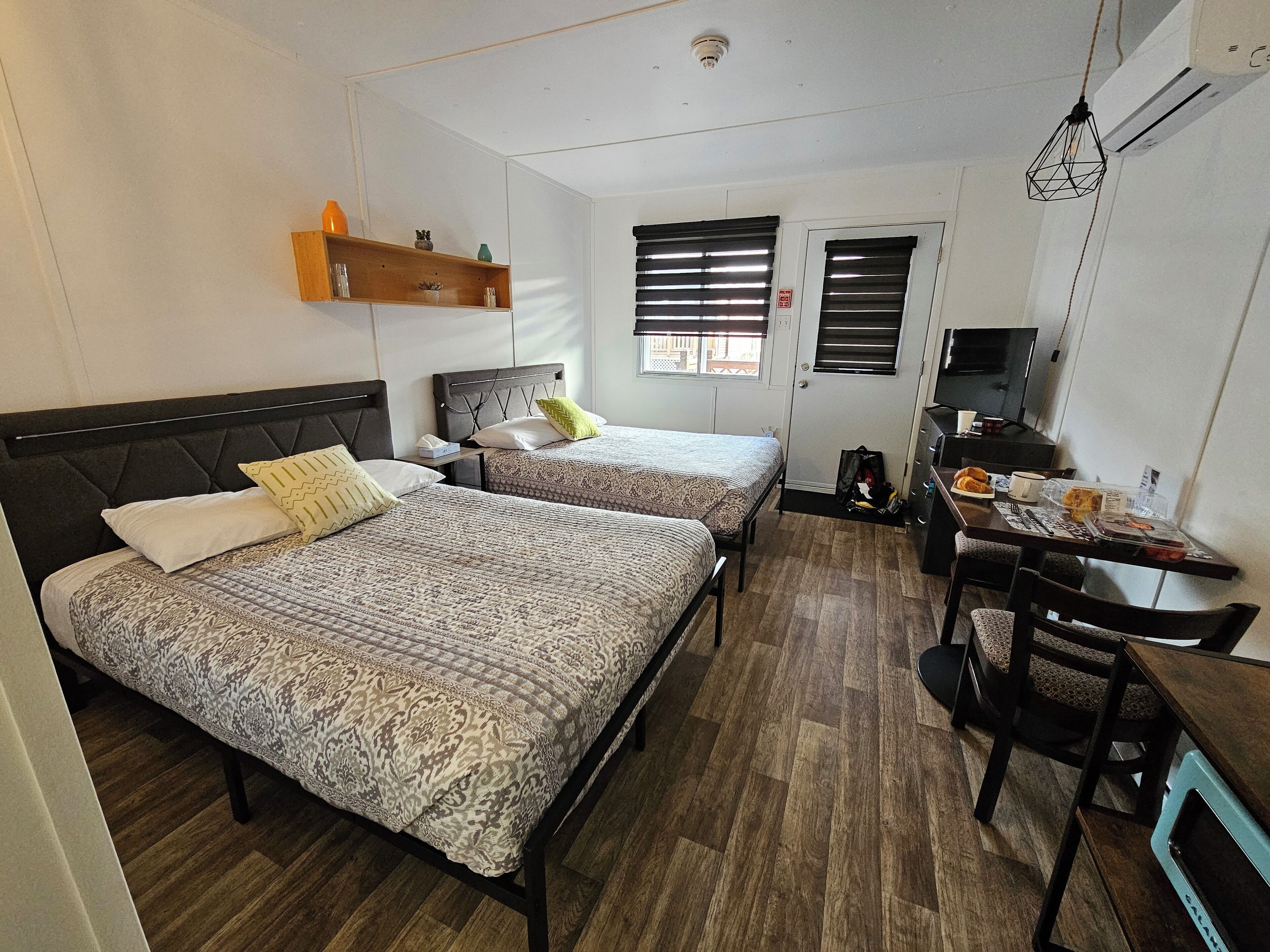 Una habitación con dos camas, un escritorio con una silla, un televisor y una estantería con objetos.