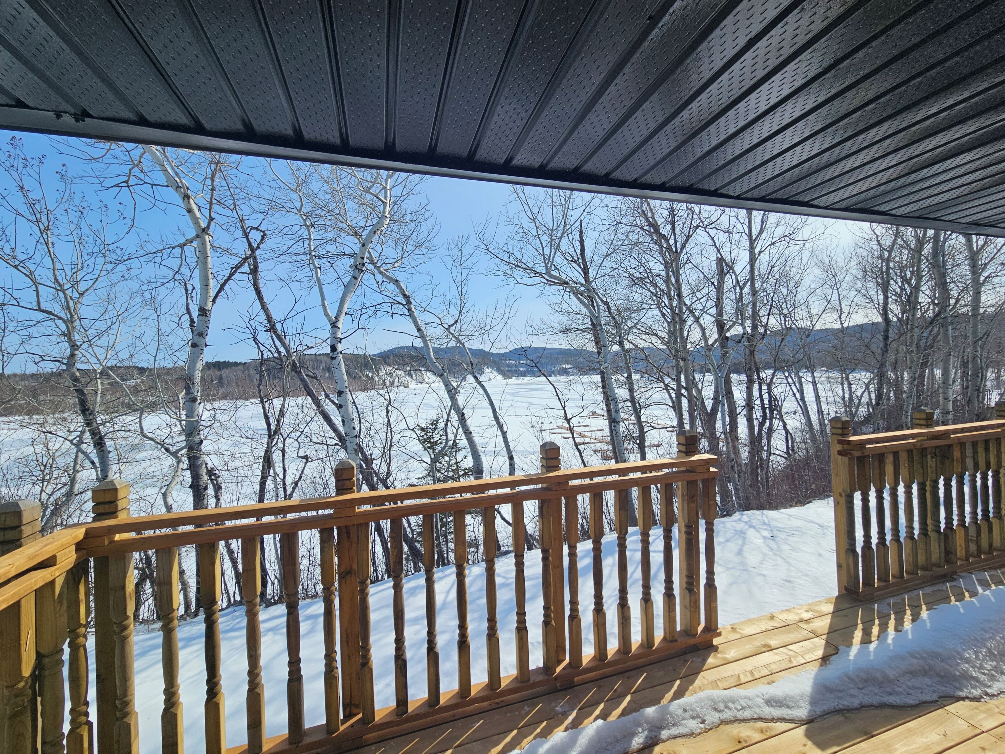 A wooden deck with a railing overlooking a snowy landscape with trees and distant hills.