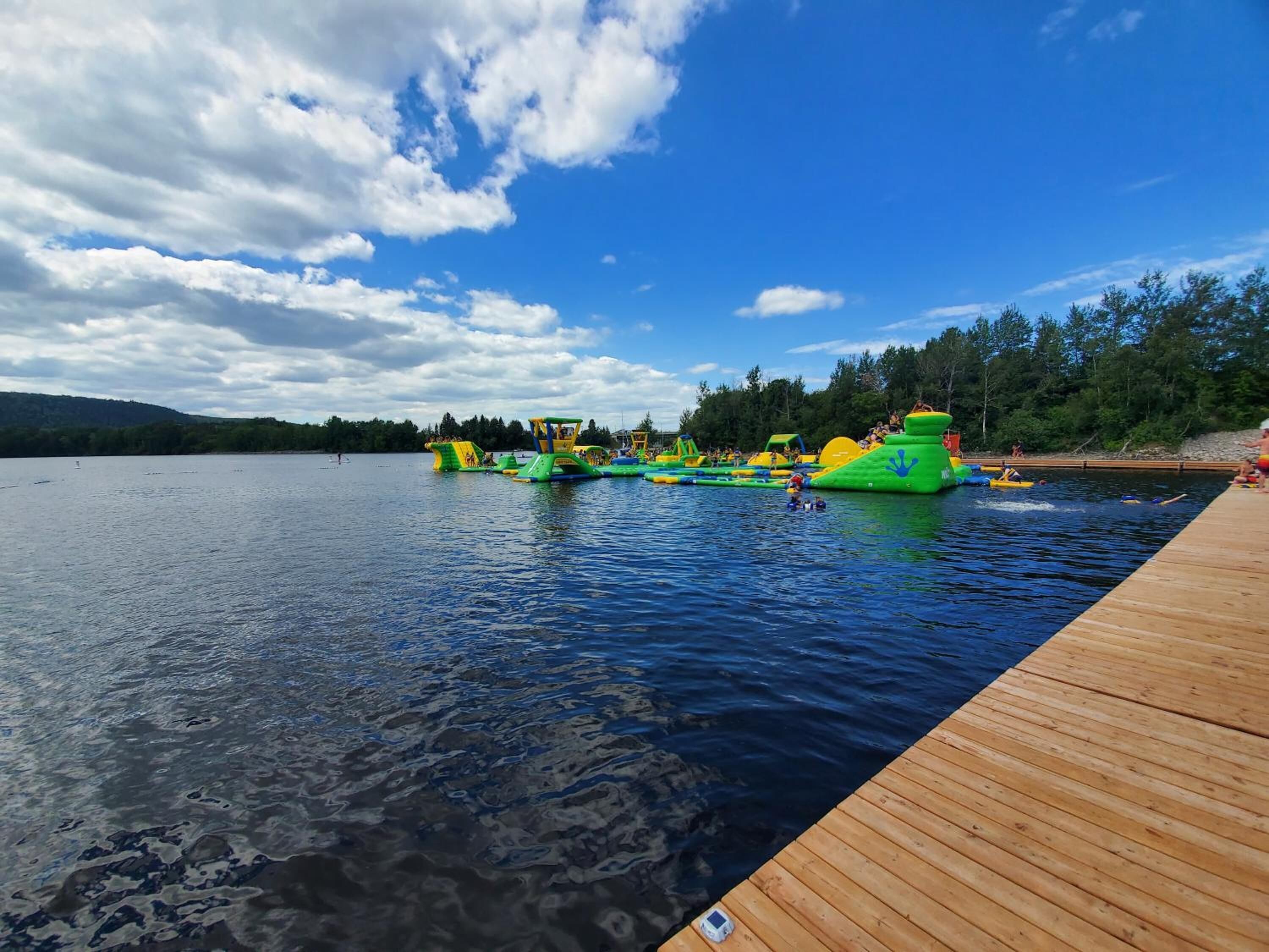 Un muelle de madera que se adentra en un lago, con estructuras flotantes para juegos acuáticos.