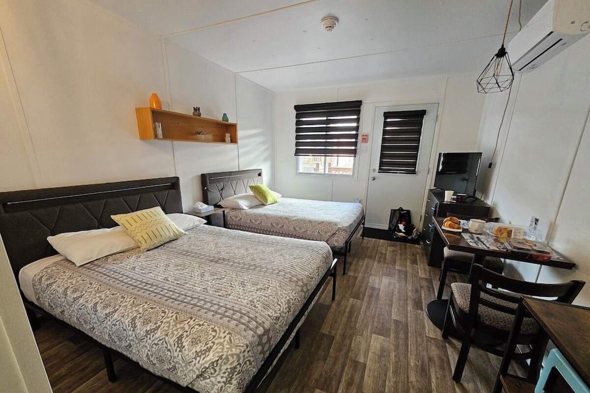 Habitación de hotel con dos camas, un escritorio, una silla, un televisor y una ventana con persianas.