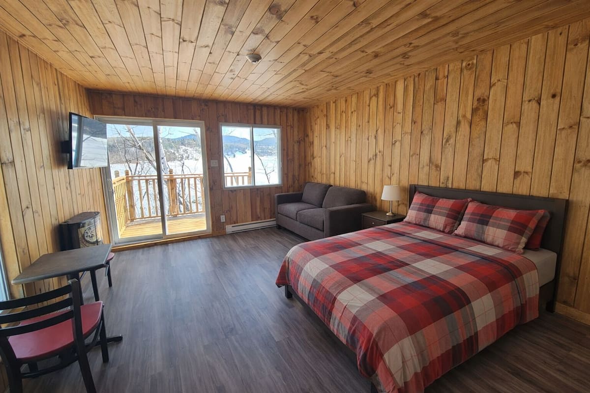 Ein Zimmer mit Holzwänden, einem Bett, einer Couch, einem Fernseher und einem Tisch.