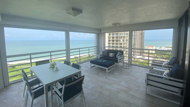 Un balcón amplio con una mesa de comedor y sillas, un sofá y una mesita auxiliar. El balcón ofrece vistas a la playa y al paisaje urbano.