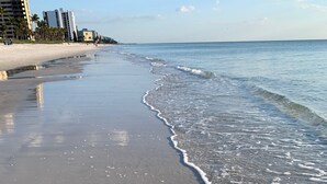 Una playa con agua cristalina, huellas y edificios al fondo.
