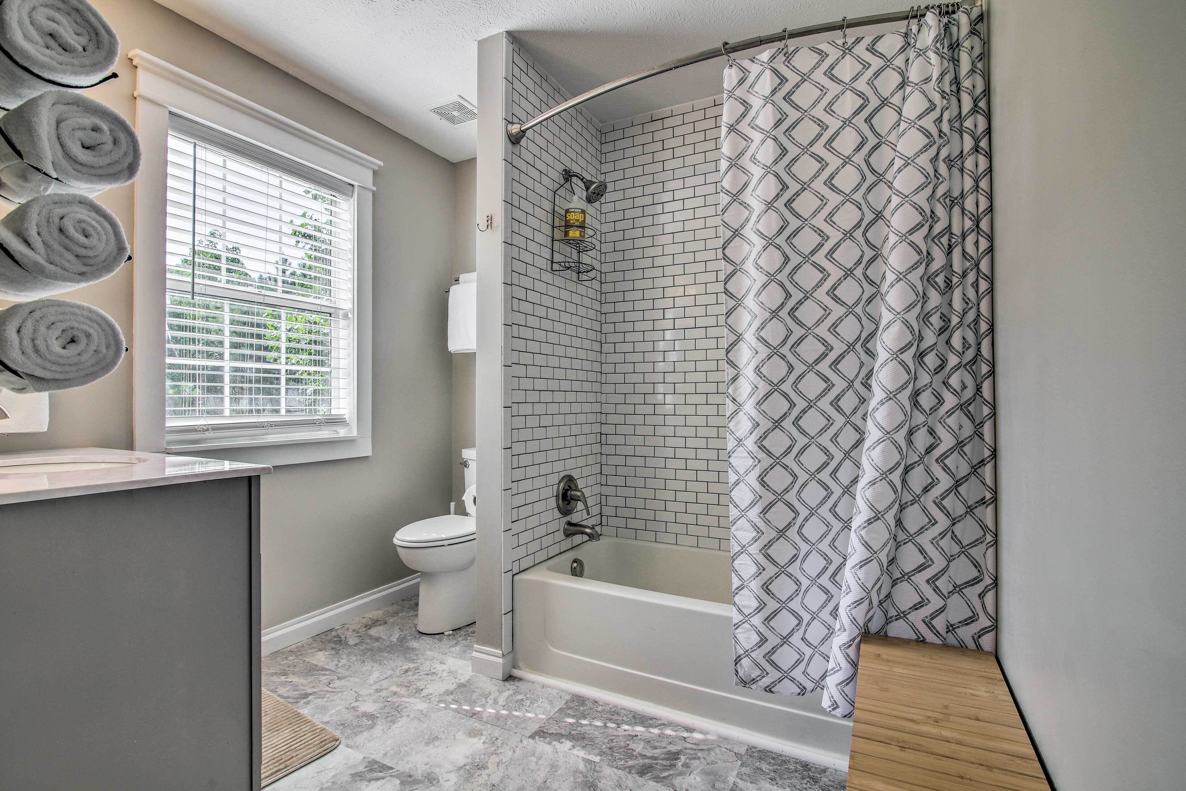 A bathroom with a bathtub, a toilet, and a window with blinds.