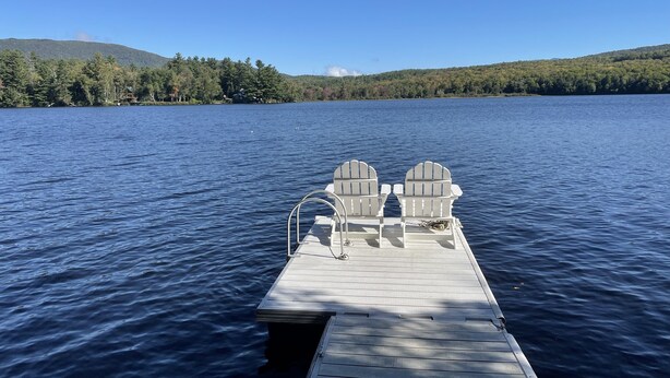 A wooden dock extending into a lake with two Adirondack chairs facing the water. - Lovelyt one bedroom nestled in the white mountains and the lakes region of NH (ORFORD)