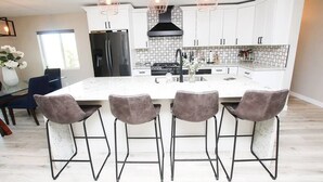Una cocina moderna con armarios blancos, una isla grande con taburetes de bar, un refrigerador negro y luces colgantes.