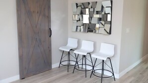 Una habitación con una puerta de madera estilo granero, tres taburetes blancos y un espejo de pared con diseño geométrico.