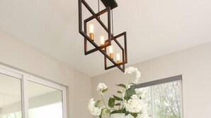 Un comedor moderno con una mesa de vidrio, sillas tapizadas en azul, una lámpara decorativa y un jarrón con flores blancas.