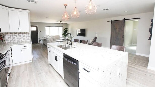 Una cocina moderna con muebles blancos, una isla grande, electrodomésticos de acero inoxidable e iluminación colgante.