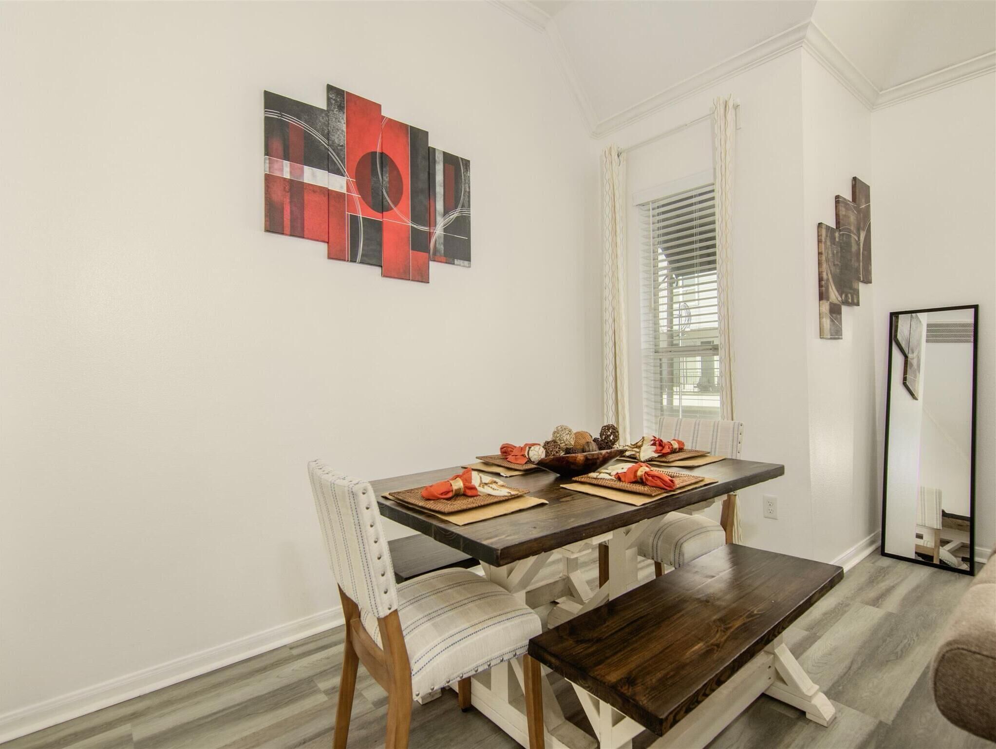 Un coin repas avec une table en bois, des chaises à revêtement blanc et un banc. Un élément décoratif orne le mur au-dessus de la table.