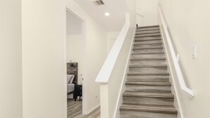 Una escalera con escalones de madera y barandillas blancas que lleva a un dormitorio con una cama y una mesita de noche.