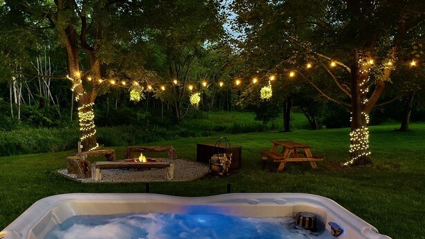 Un bain à remous entouré d’arbres, un foyer et des tables de pique-nique.