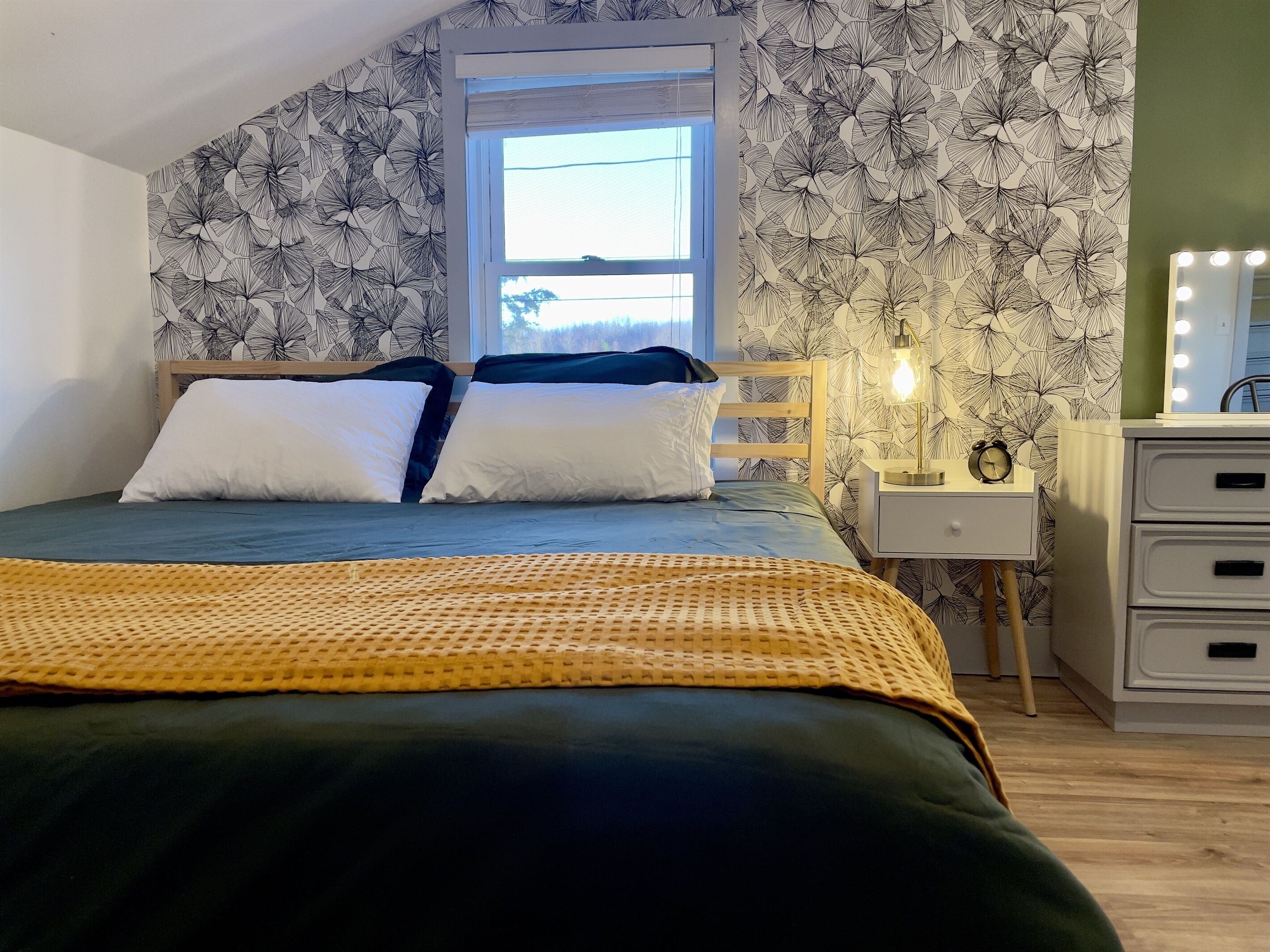 Un dormitorio con cama, mesita de noche, cómoda y ventana.
