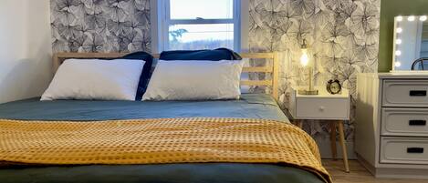 Un dormitorio con cama, mesita de noche, cómoda y ventana.